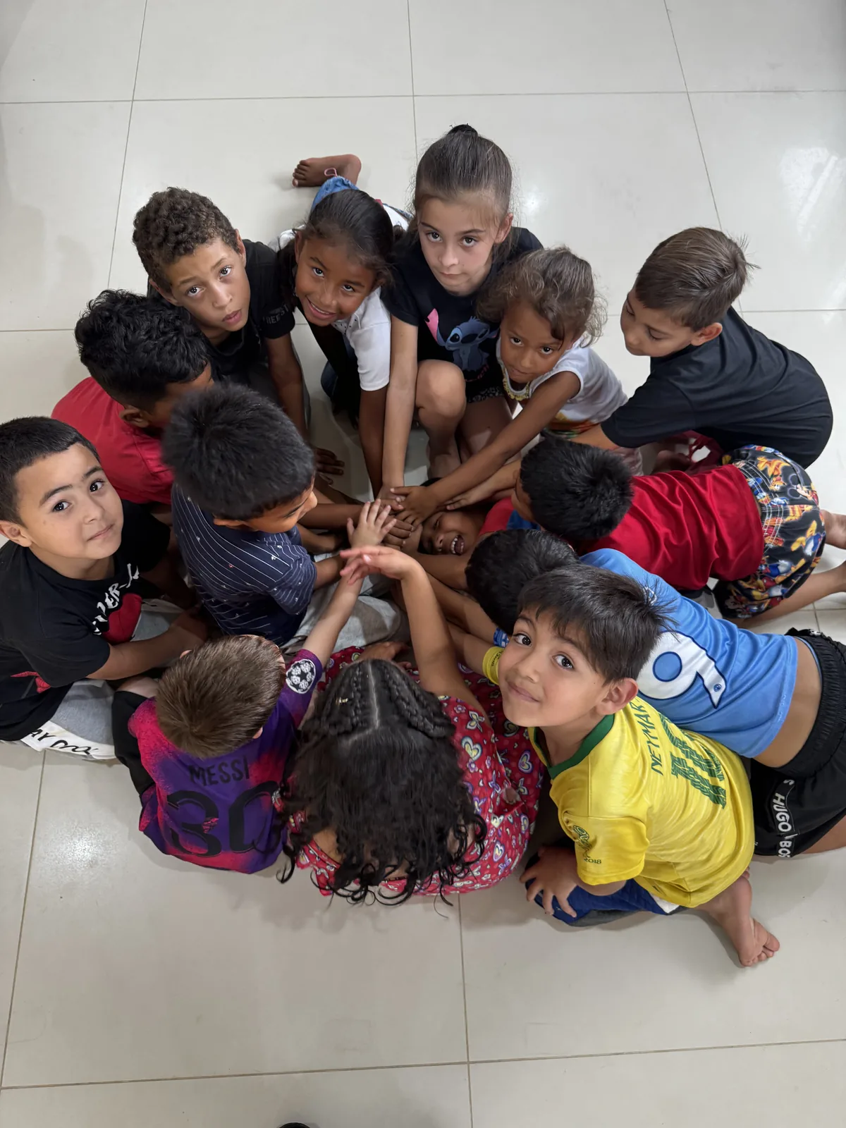 Crianças atendidas pela Biblioteca Amigos do Caximba reunidas em roda, com as mãos no centro, olhando para a câmera.