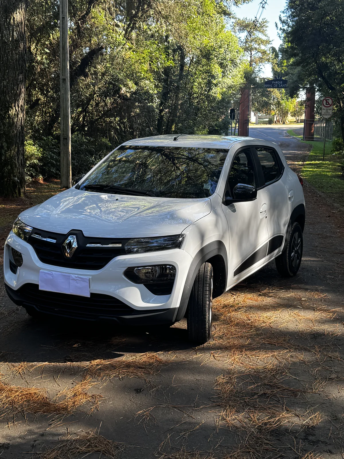 Renault Kwid 0km branco, em ângulo frontal, estacionado em uma área arborizada.