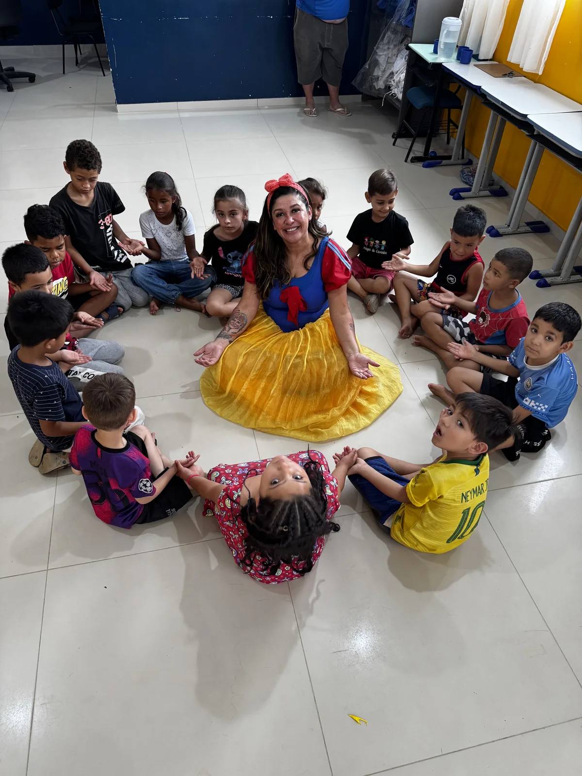 Tia Edi sentada em roda com as crianças atendidas pela Biblioteca Amigos do Caximba.